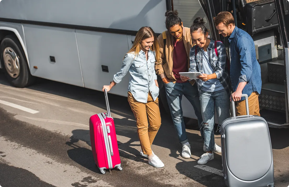 Young travellers with suitcases beside a coach, looking at their booking on a tablet